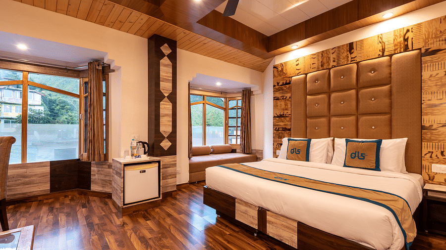 A hotel room in Bhagsunag featuring a large bed, wooden floors, a wooden ceiling, and windows with a view - DLS Meghavan Resort